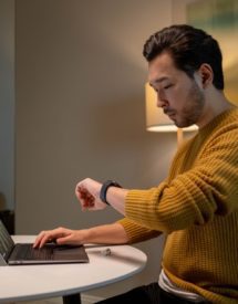 A person looking at a watch while working on a laptop